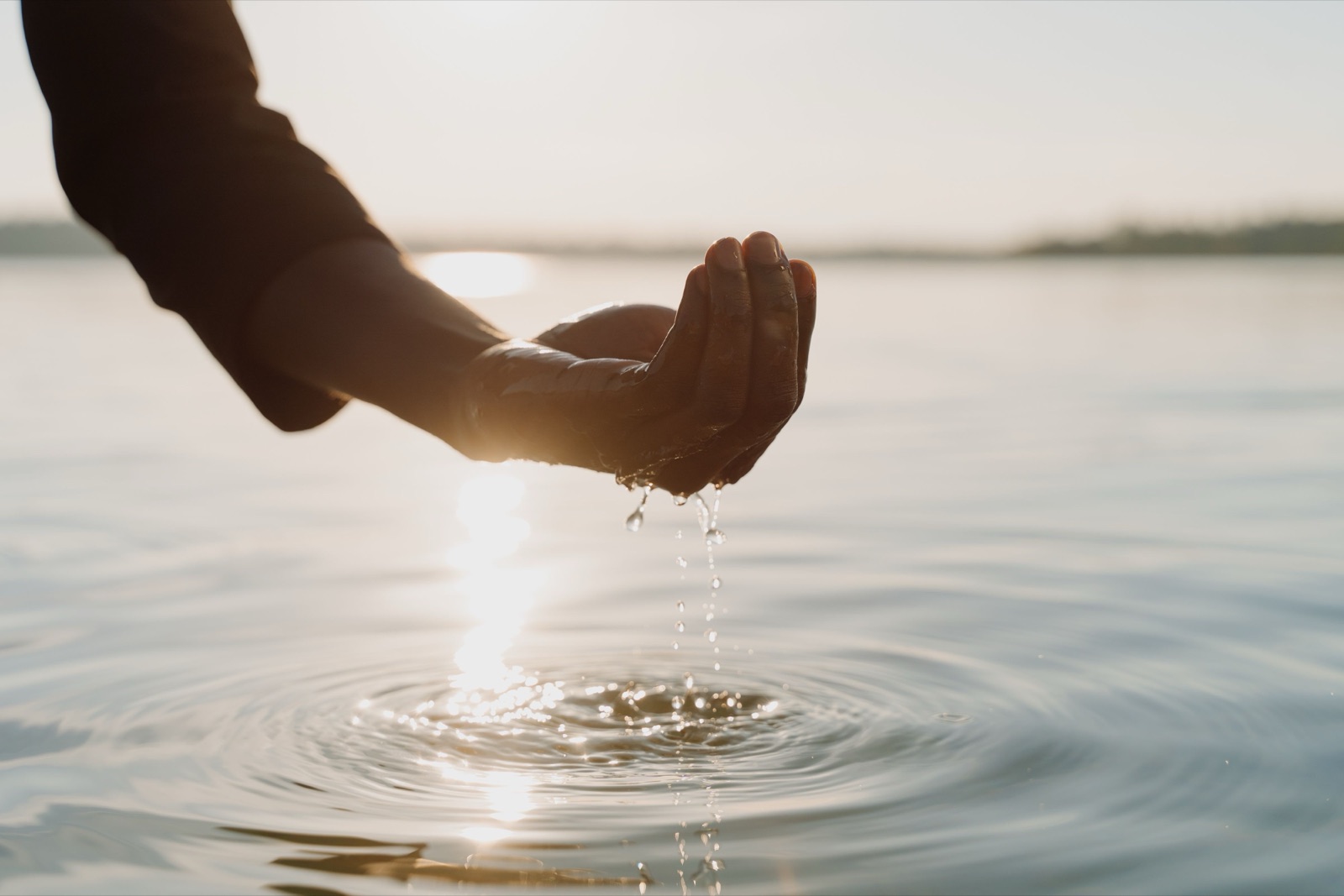 A hand holding flowing water in warm sunlight.