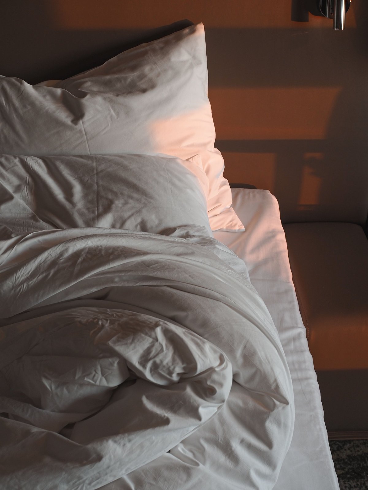 An unmade bed with white pillows and rumpled sheets in warm light.
